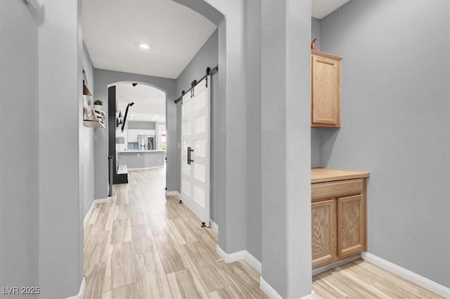 corridor with baseboards, a barn door, light wood finished floors, and arched walkways
