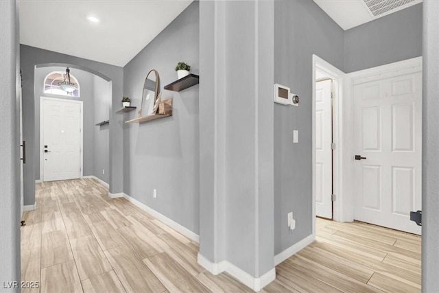 entrance foyer featuring arched walkways, baseboards, visible vents, and light wood finished floors