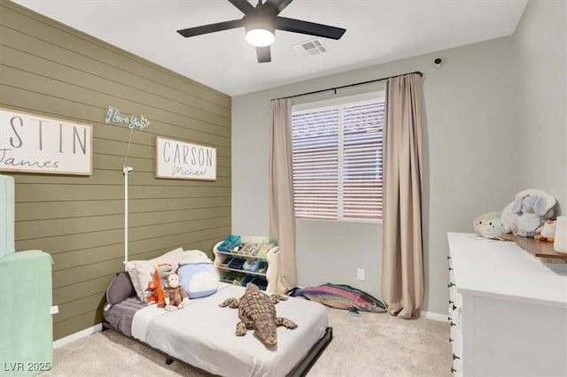 carpeted bedroom with wooden walls, baseboards, a ceiling fan, and visible vents