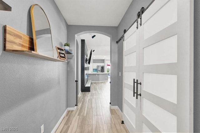 hall featuring light wood-style floors, baseboards, arched walkways, and a barn door