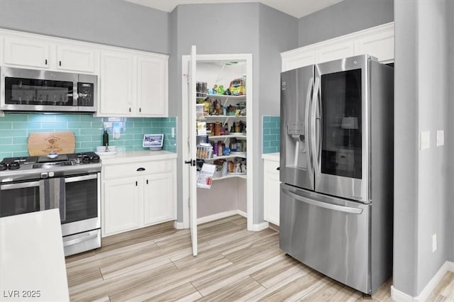 kitchen with backsplash, appliances with stainless steel finishes, white cabinetry, light countertops, and light wood-style flooring