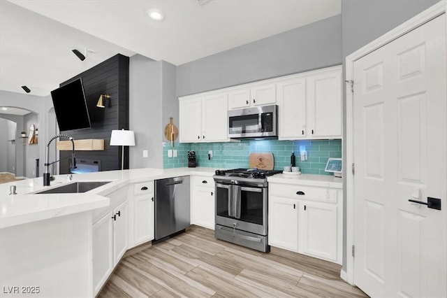 kitchen with white cabinets, appliances with stainless steel finishes, a sink, a peninsula, and tasteful backsplash