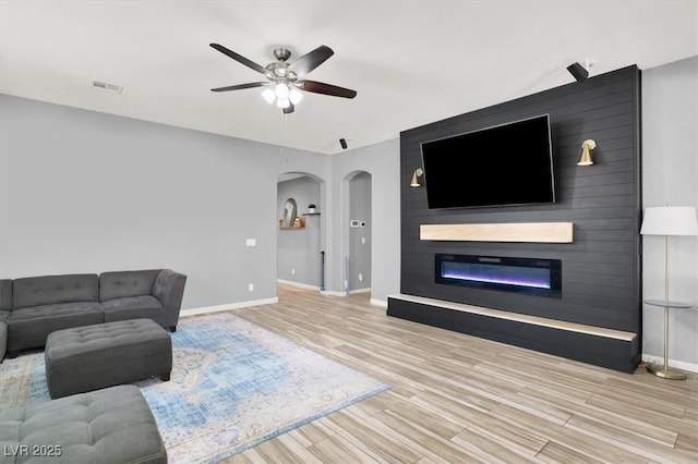 living room with a ceiling fan, arched walkways, a large fireplace, wood finished floors, and baseboards