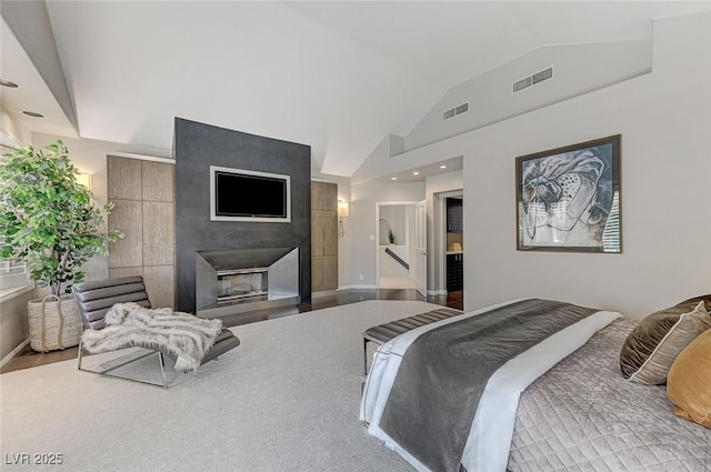 bedroom with visible vents, a glass covered fireplace, wood finished floors, and vaulted ceiling