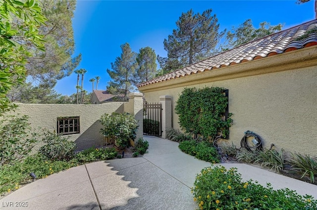 view of exterior entry with a tiled roof, a gate, and stucco siding