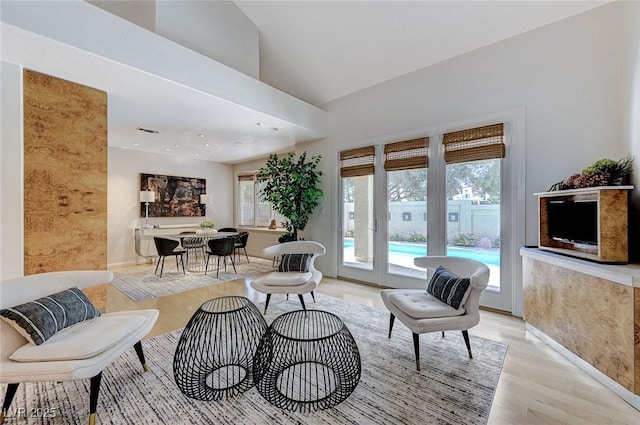living area featuring light wood-style floors, vaulted ceiling, and visible vents