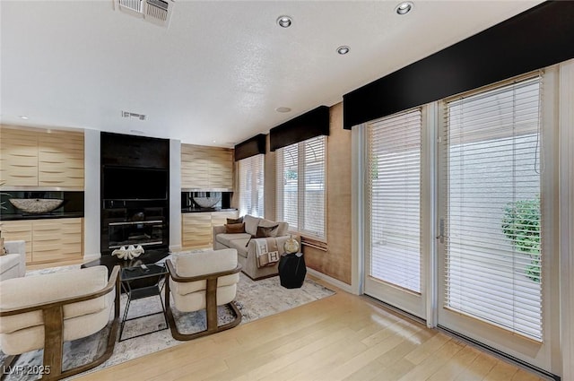 living room featuring visible vents, baseboards, a multi sided fireplace, and light wood-type flooring
