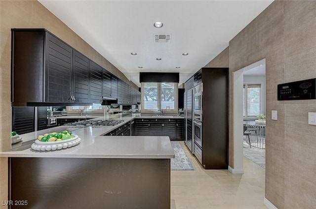 kitchen featuring visible vents, a peninsula, light countertops, a sink, and appliances with stainless steel finishes