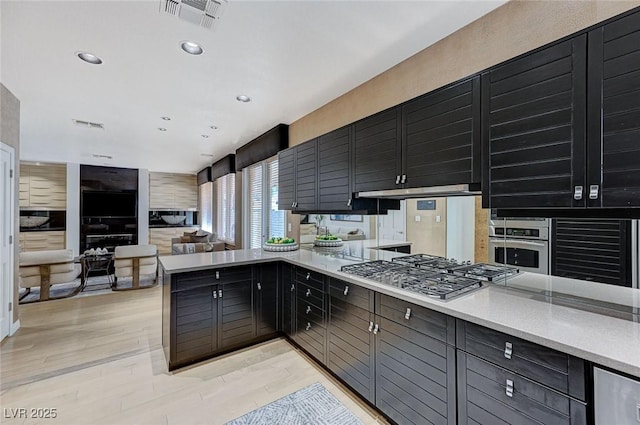 kitchen featuring visible vents, a peninsula, light wood-type flooring, light countertops, and appliances with stainless steel finishes
