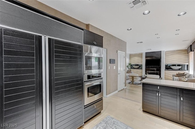 kitchen with visible vents, built in appliances, open floor plan, light countertops, and light wood finished floors