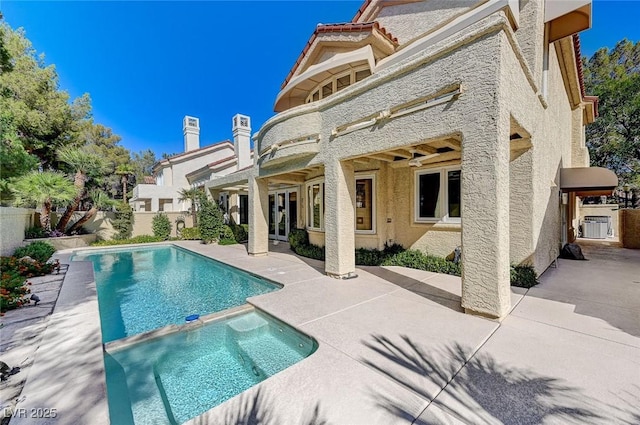 rear view of property with french doors, a pool with connected hot tub, fence, a patio, and stucco siding
