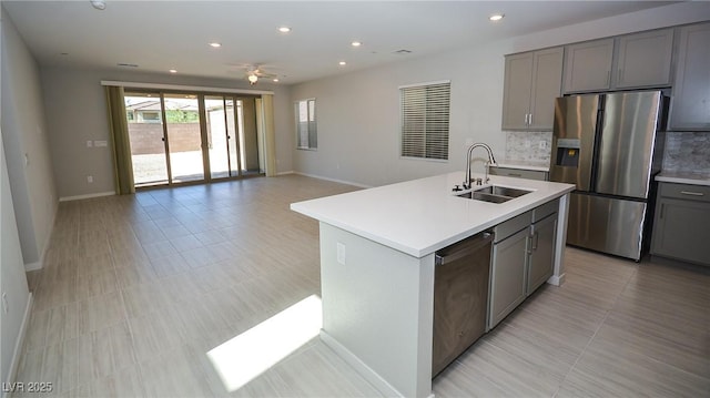 kitchen with appliances with stainless steel finishes, a sink, light countertops, gray cabinets, and decorative backsplash