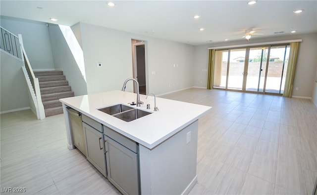 kitchen with a sink, a kitchen island with sink, gray cabinets, a ceiling fan, and stainless steel dishwasher
