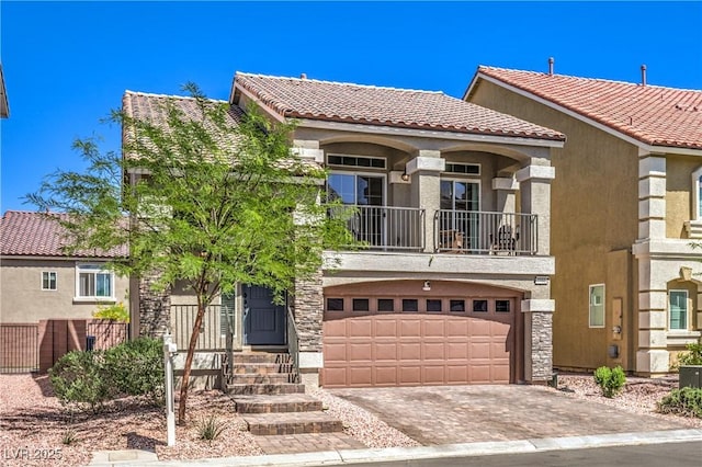 mediterranean / spanish house with a garage, a balcony, decorative driveway, stucco siding, and a tiled roof