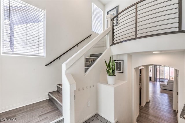 stairs with arched walkways, baseboards, and wood finished floors