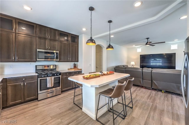 kitchen featuring dark brown cabinetry, appliances with stainless steel finishes, light wood-style floors, a breakfast bar area, and arched walkways