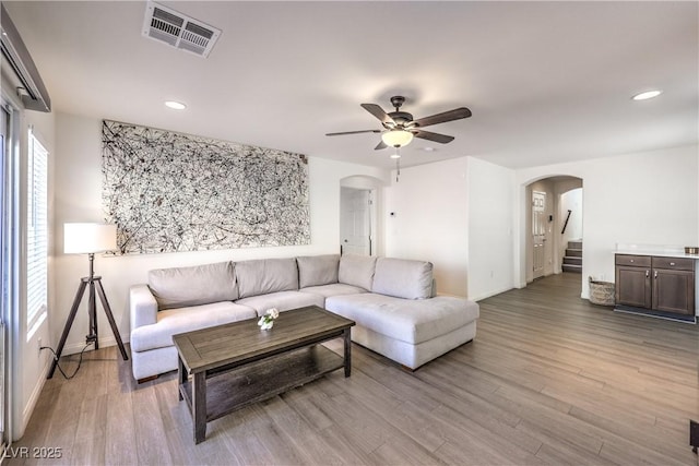 living room featuring ceiling fan, visible vents, arched walkways, light wood-type flooring, and baseboards
