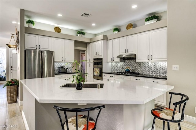 kitchen featuring visible vents, appliances with stainless steel finishes, tasteful backsplash, a breakfast bar, and under cabinet range hood