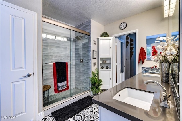 full bath featuring a sink, double vanity, a shower stall, and a textured ceiling
