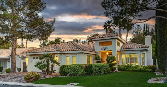 mediterranean / spanish-style house with an attached garage, stucco siding, a tiled roof, a yard, and driveway