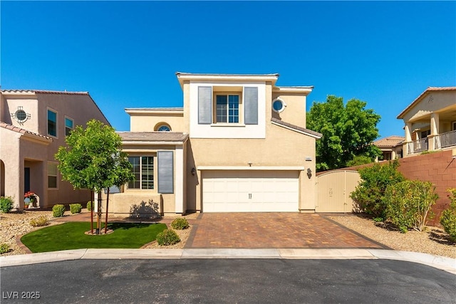 traditional-style house featuring a garage, fence, stucco siding, and decorative driveway