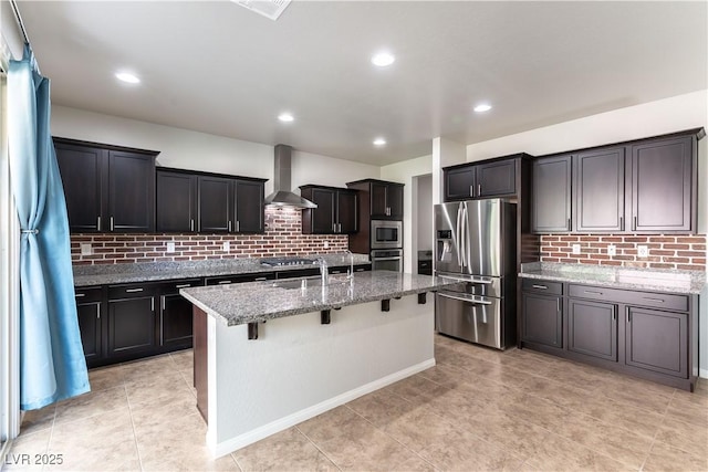 kitchen featuring light stone countertops, appliances with stainless steel finishes, a breakfast bar area, wall chimney exhaust hood, and tasteful backsplash
