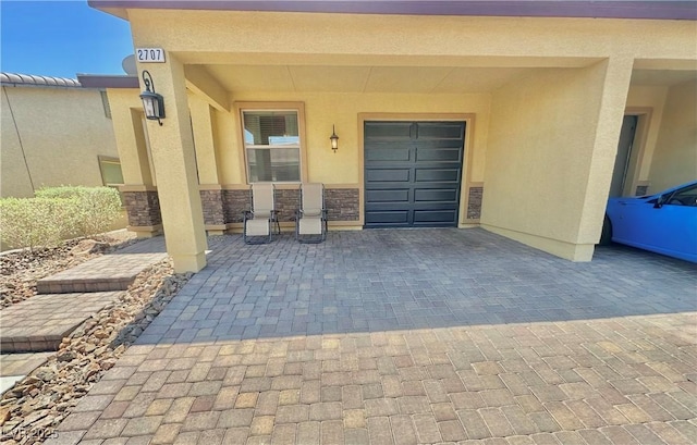 property entrance with decorative driveway, a garage, stone siding, and stucco siding