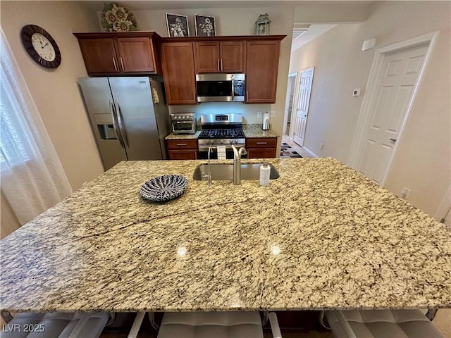 kitchen featuring a breakfast bar area, light stone countertops, a spacious island, a sink, and stainless steel appliances