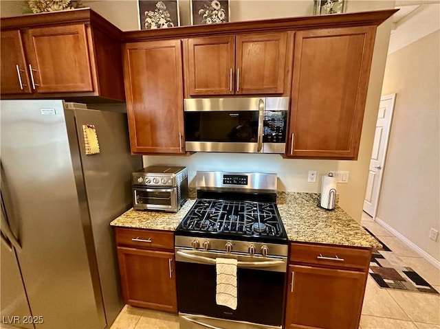 kitchen with stainless steel appliances, light stone counters, brown cabinetry, and light tile patterned floors