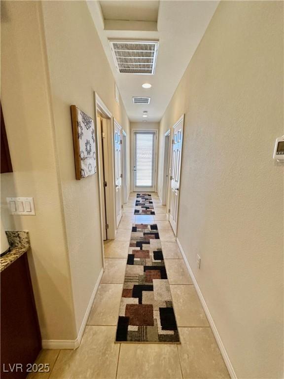 corridor with light tile patterned flooring, baseboards, and visible vents