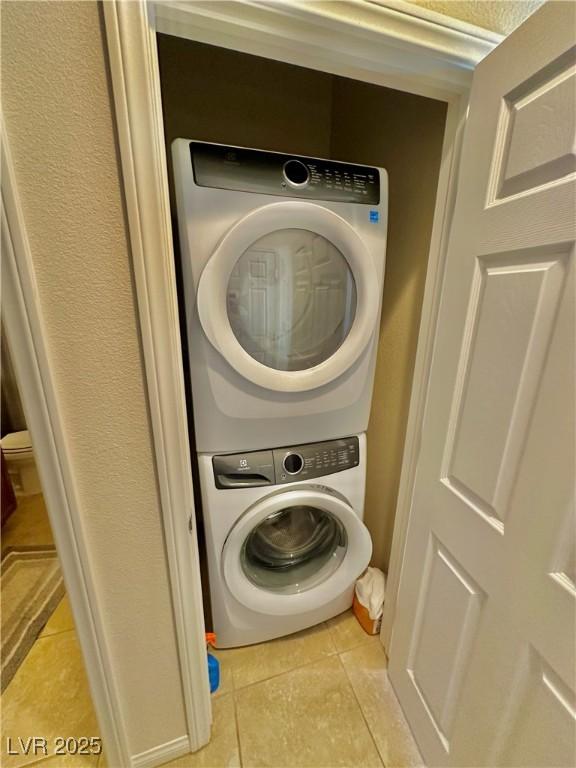 washroom with stacked washer / drying machine and light tile patterned flooring