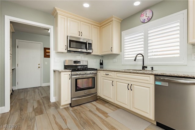 kitchen with a sink, appliances with stainless steel finishes, light wood-style flooring, and cream cabinetry
