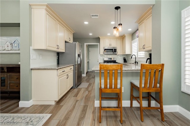 kitchen featuring appliances with stainless steel finishes, a sink, light stone counters, a peninsula, and light wood finished floors