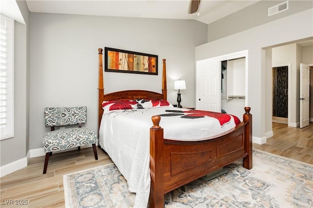 bedroom featuring visible vents, a closet, baseboards, light wood finished floors, and vaulted ceiling