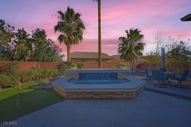 patio terrace at dusk with an outdoor hot tub and a fenced backyard