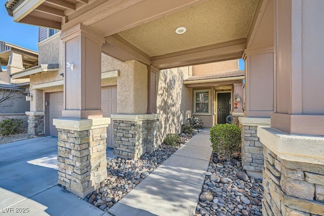 entrance to property with stucco siding, an attached garage, and stone siding
