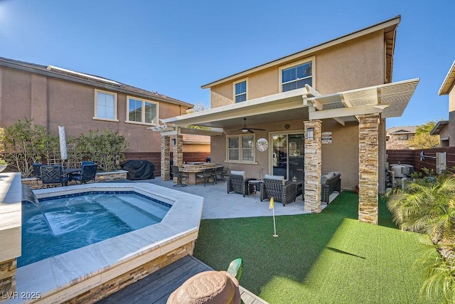 rear view of property with ceiling fan, fence, stucco siding, a patio area, and a jacuzzi