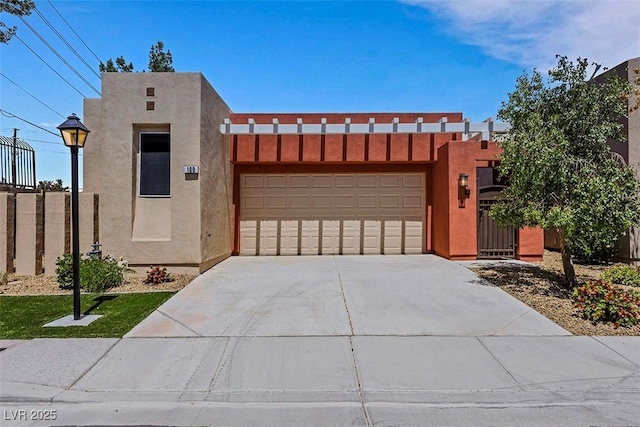 pueblo-style home with concrete driveway, fence, stucco siding, and a garage