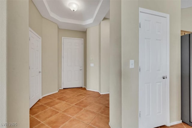 hall with baseboards, a raised ceiling, and light tile patterned floors