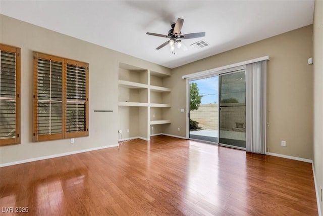 unfurnished living room featuring built in shelves, a ceiling fan, baseboards, wood finished floors, and visible vents