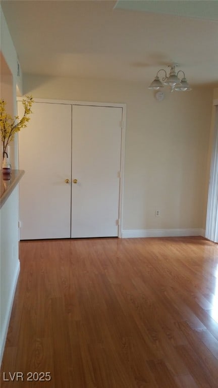 unfurnished bedroom featuring baseboards, a chandelier, and wood finished floors