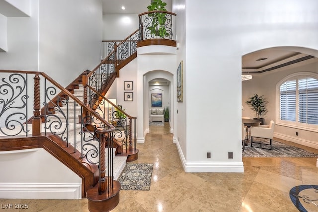 foyer featuring baseboards, arched walkways, and stairs