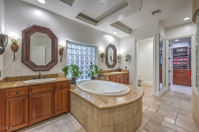 full bathroom with stone tile floors, visible vents, a sink, and a jetted tub