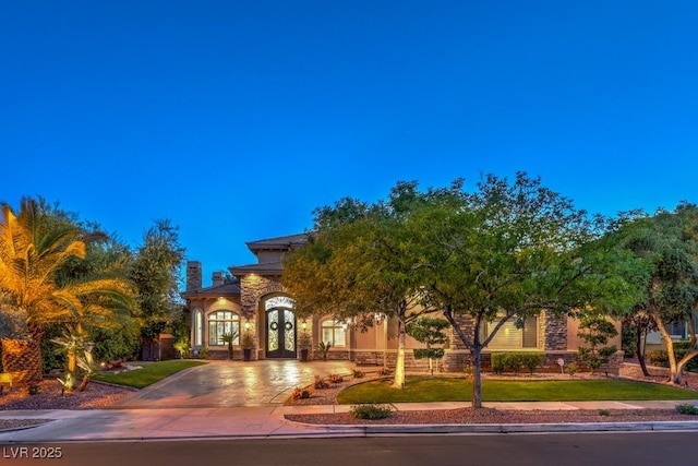 view of front facade featuring curved driveway, french doors, and stone siding