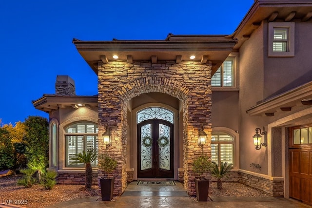 property entrance featuring french doors, stucco siding, and stone siding