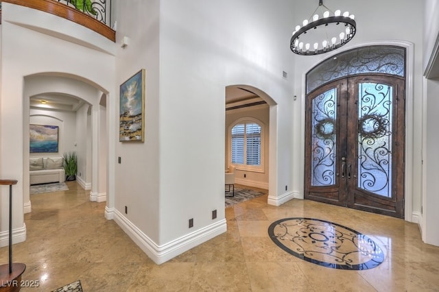 entrance foyer with baseboards, arched walkways, a high ceiling, and french doors