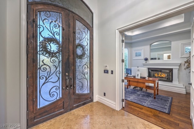 tiled foyer entrance with baseboards, a glass covered fireplace, ornamental molding, and french doors