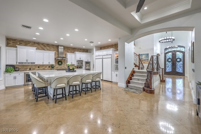 kitchen with wall chimney range hood, arched walkways, french doors, white cabinetry, and wine cooler