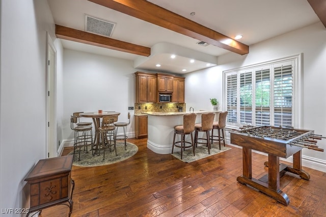 kitchen with brown cabinetry, dark wood-style flooring, visible vents, beam ceiling, and stainless steel microwave