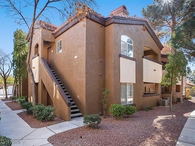 view of home's exterior featuring a tile roof, stucco siding, stairway, central AC unit, and a chimney